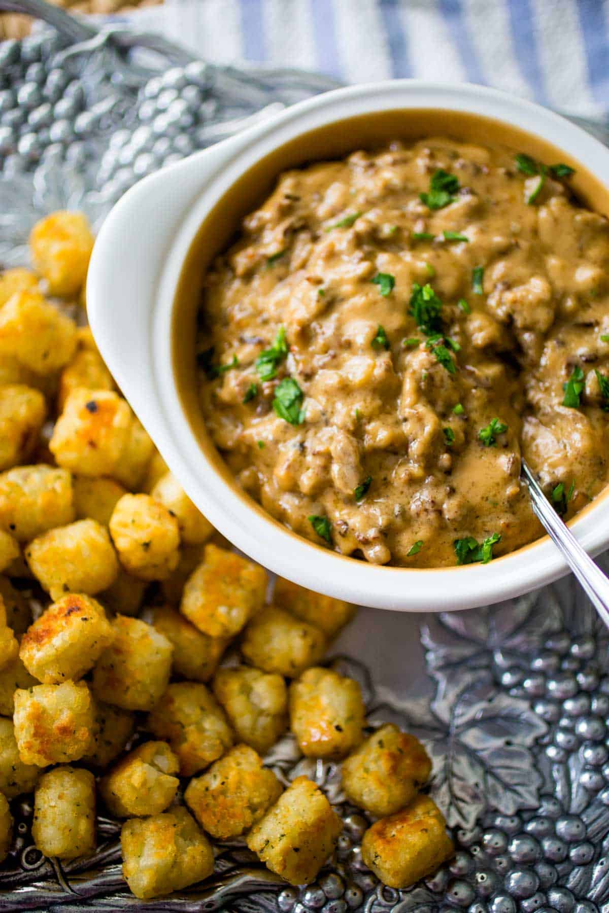 The dip is in a white serving bowl next to a platter of tater tots.