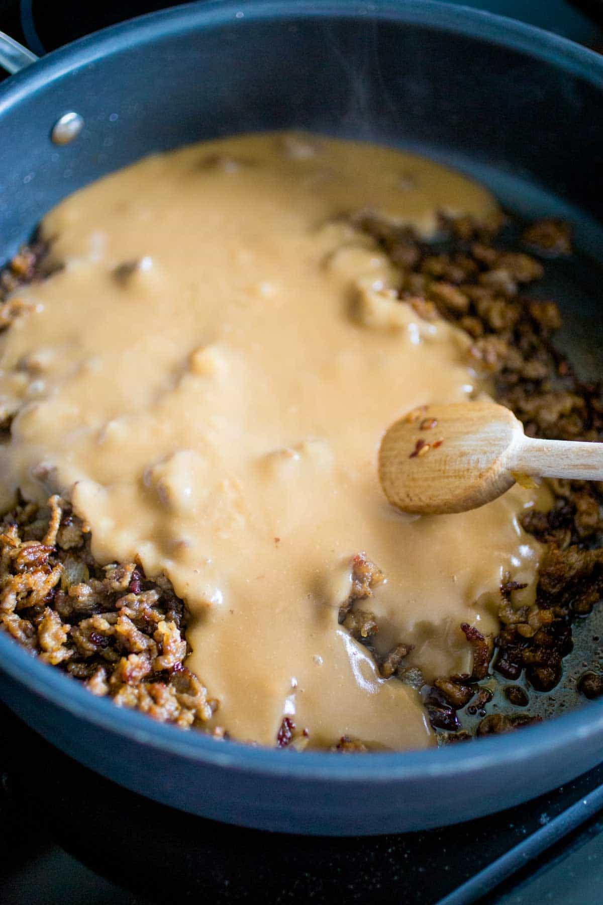 The thickened beef broth is added to the sausage in the skillet.