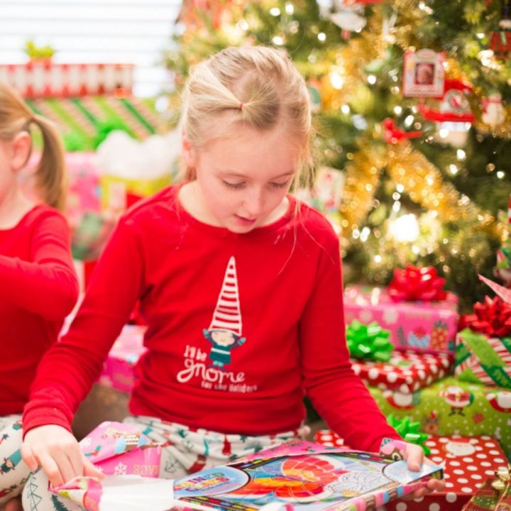 A young girl opens a gift in front of the Christmas tree on Christmas morning.