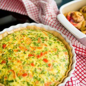 The baked quiche sits on a red and white checked kitchen towel.