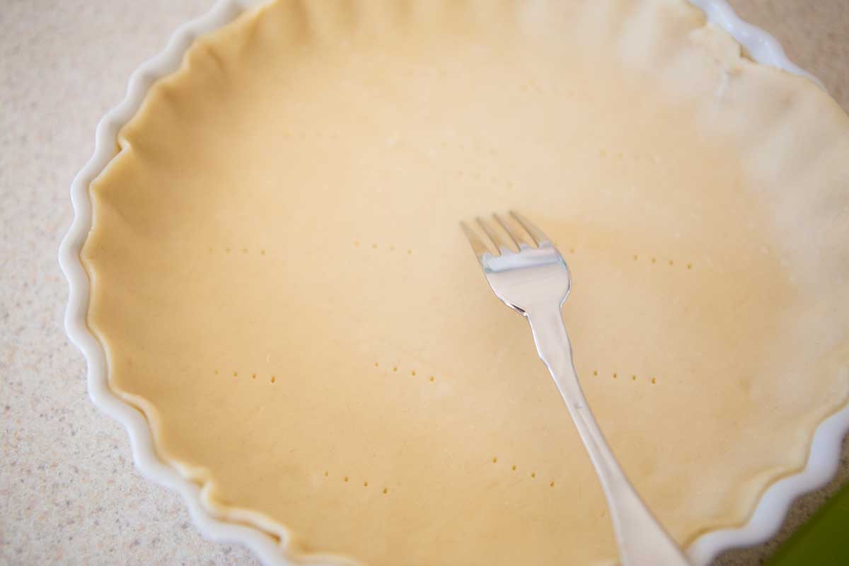 The quiche pan has been filled with Pillsbury pie crust and has a fork pricking holes in the bottom.