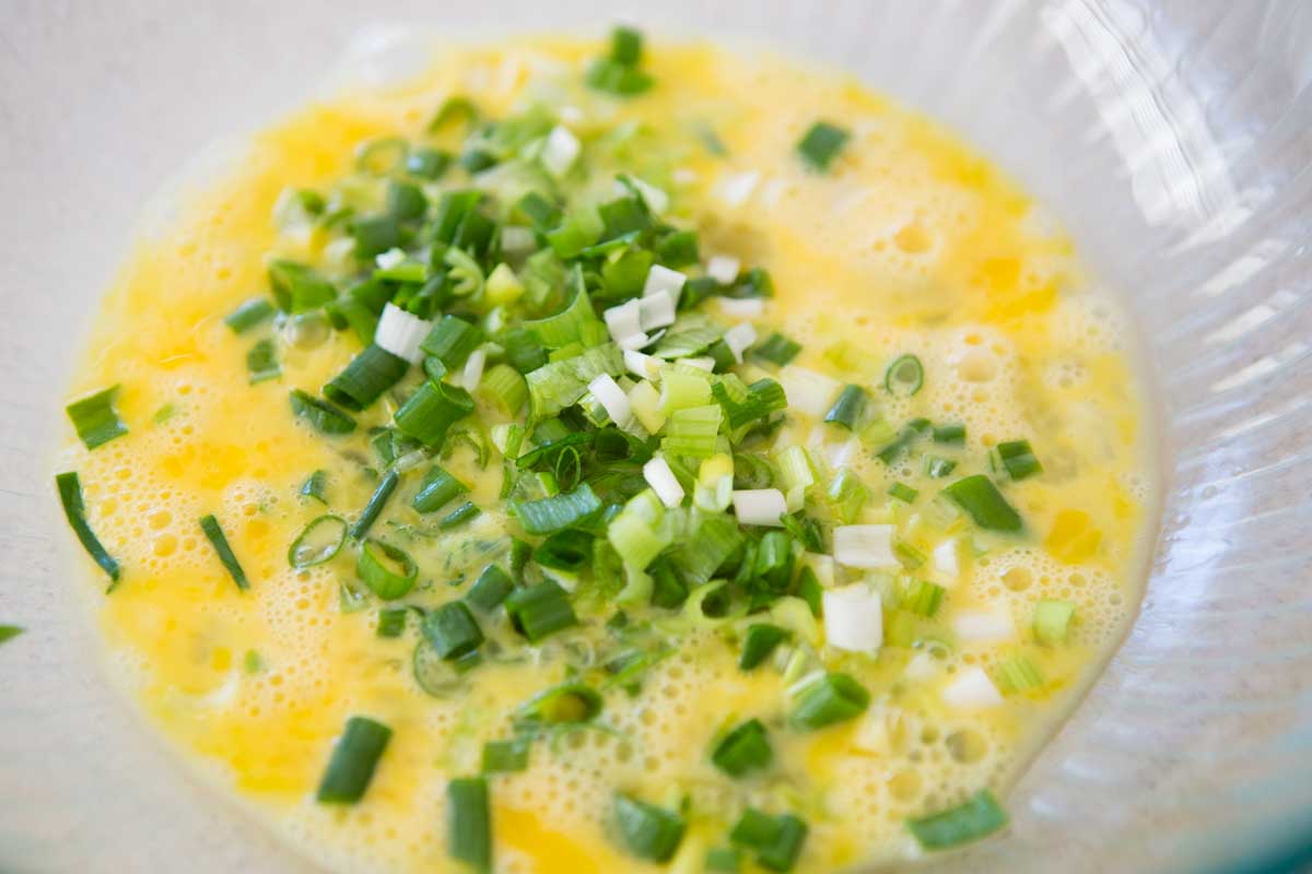 The whisked eggs and green onions are in a mixing bowl.