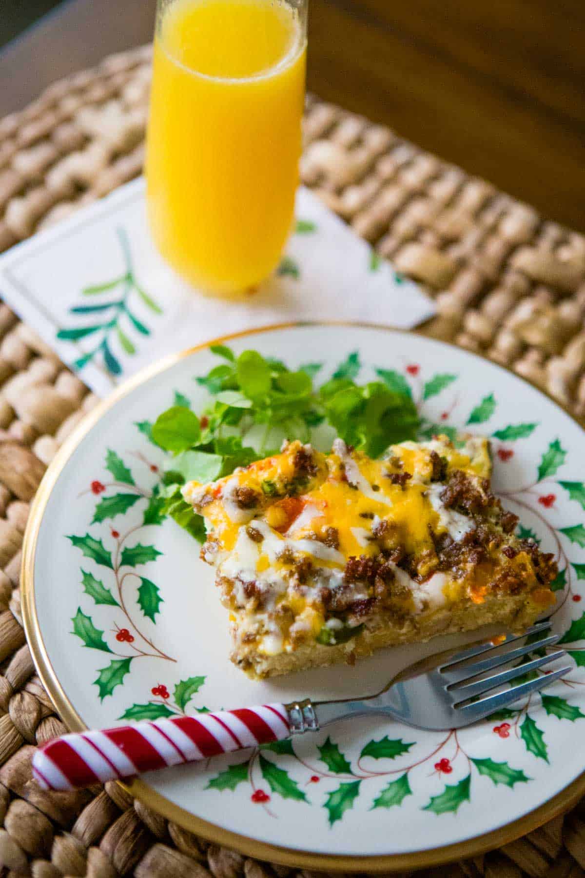 The breakfast casserole has been sliced and served on a Christmas china plate next to a mimosa.