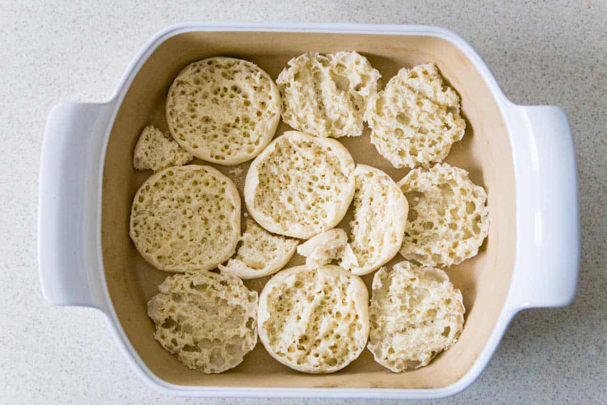 The english muffins are in a casserole dish, each one has been halved and placed cut side up.