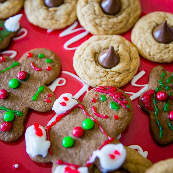A Christmas cookie platter has frosted gingerbread men and peanut blossom cookies on a red plate.