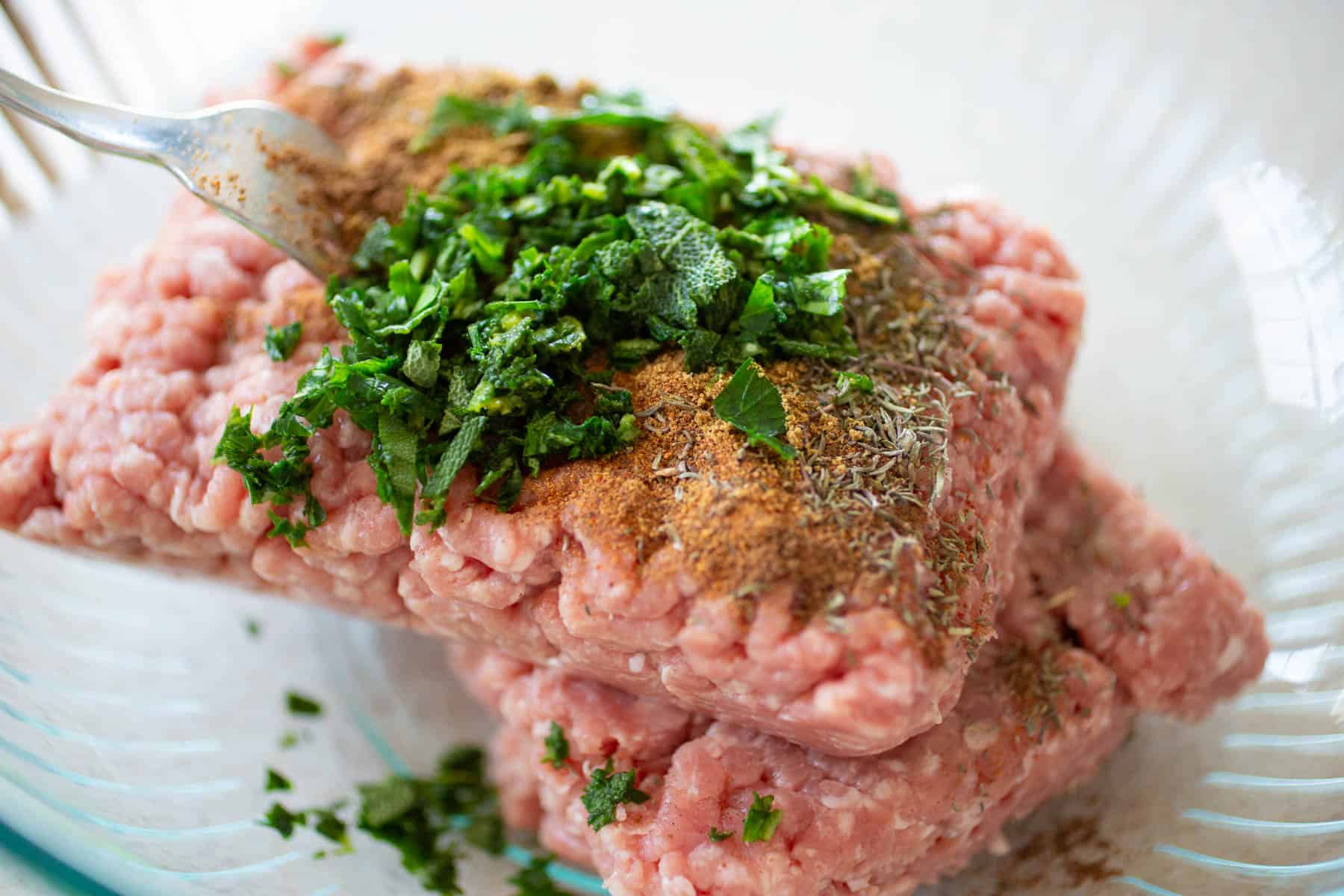 The sausage is in a mixing bowl with herbs and seasonings on top.