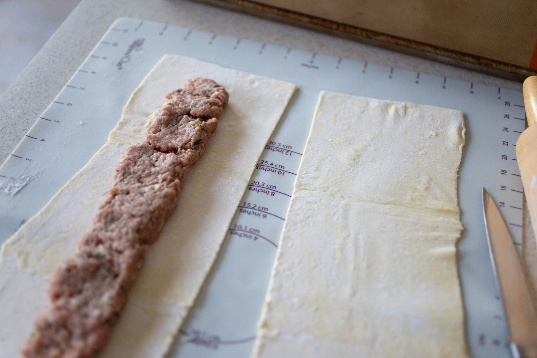 The sausage has been lined up on the pastry and is about to be rolled.