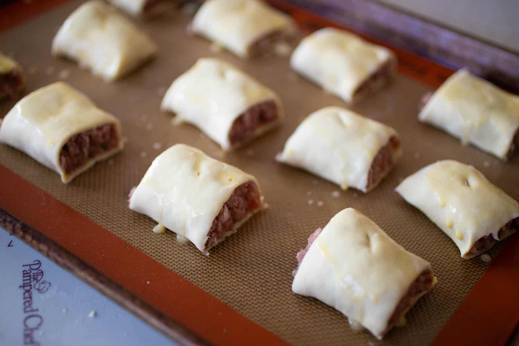 The sliced sausage rolls are on a baking sheet lined with a silicone baking mat.