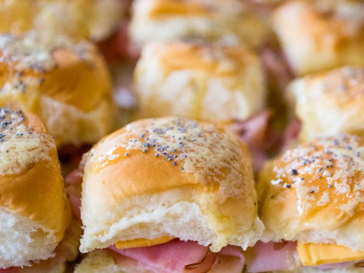 A filled baking pan of mini ham sliders with butter dripping off the top and a sprinkle of poppyseeds on each one.