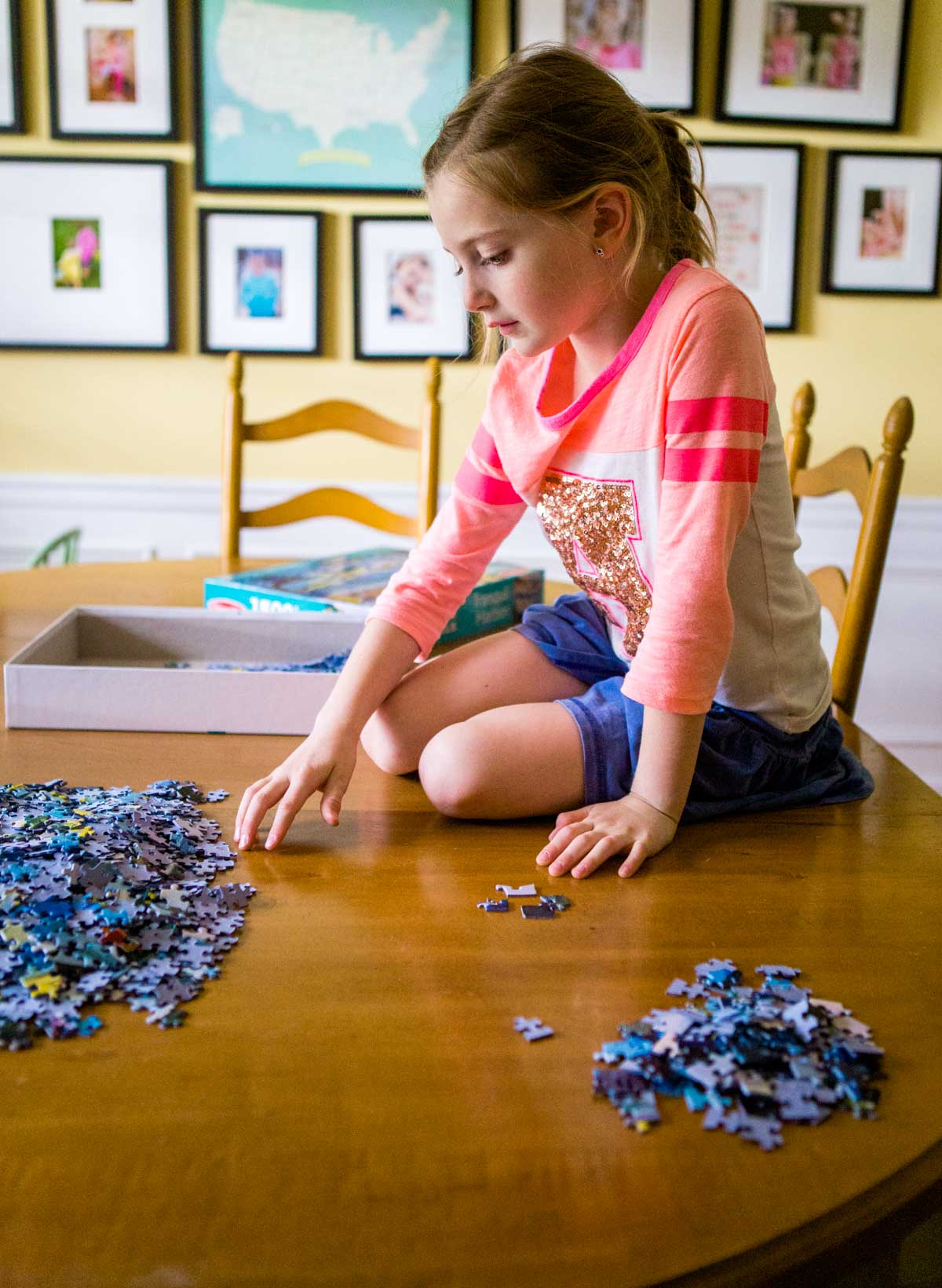A girl sits on top of the table to sort the pieces.