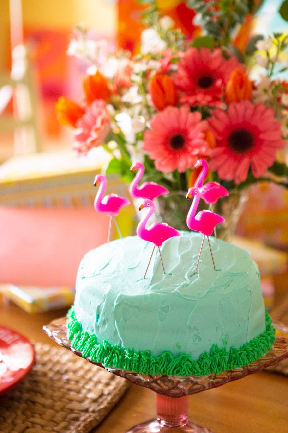A flamingo cake on a pink cake plate with flowers in the background.