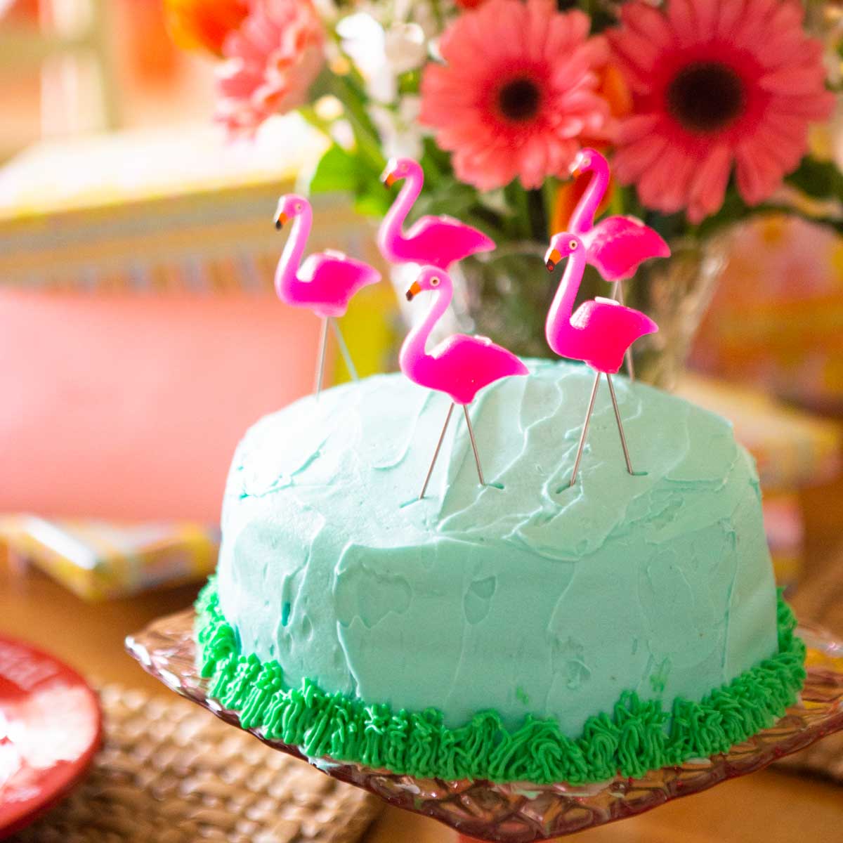 A blue birthday cake has pink flamingo candles on top.