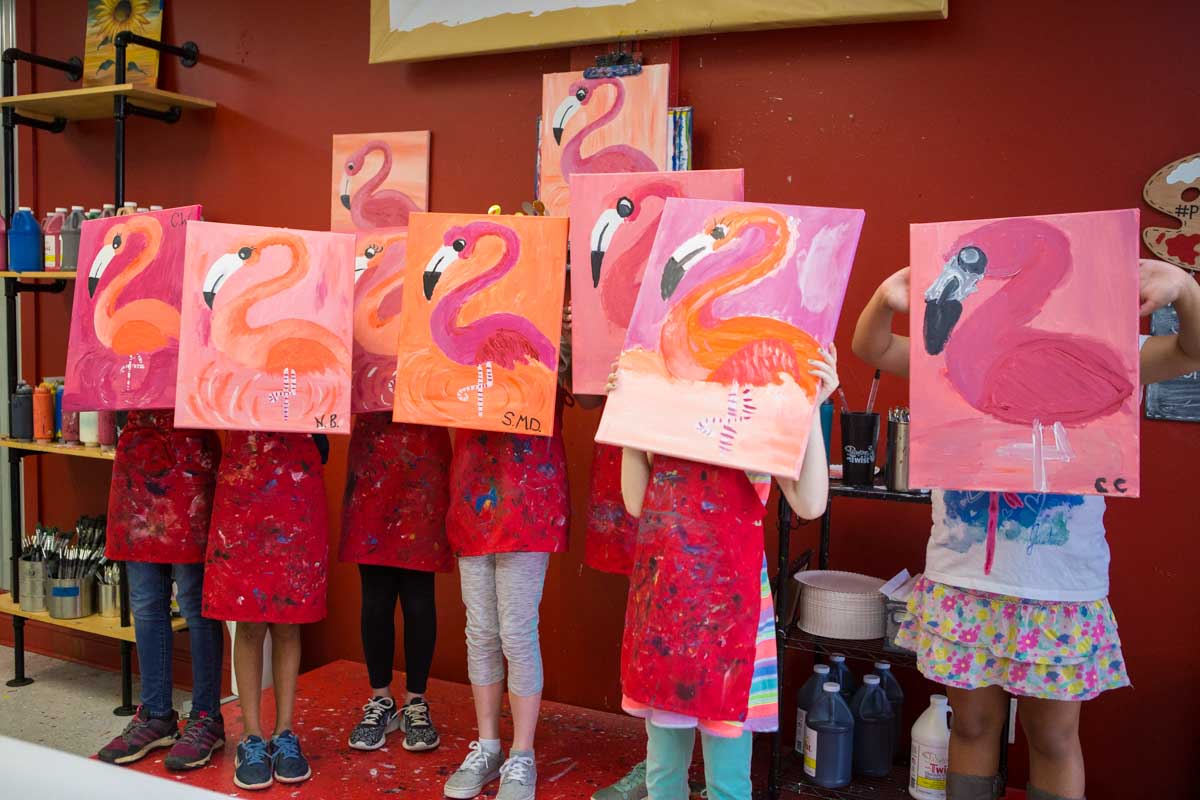 A line-up of kids holding paintings of tropical flamingos.