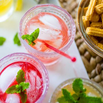 Colorful mint juleps with fresh mint sit on a platter next to a bowl of cheese straws.