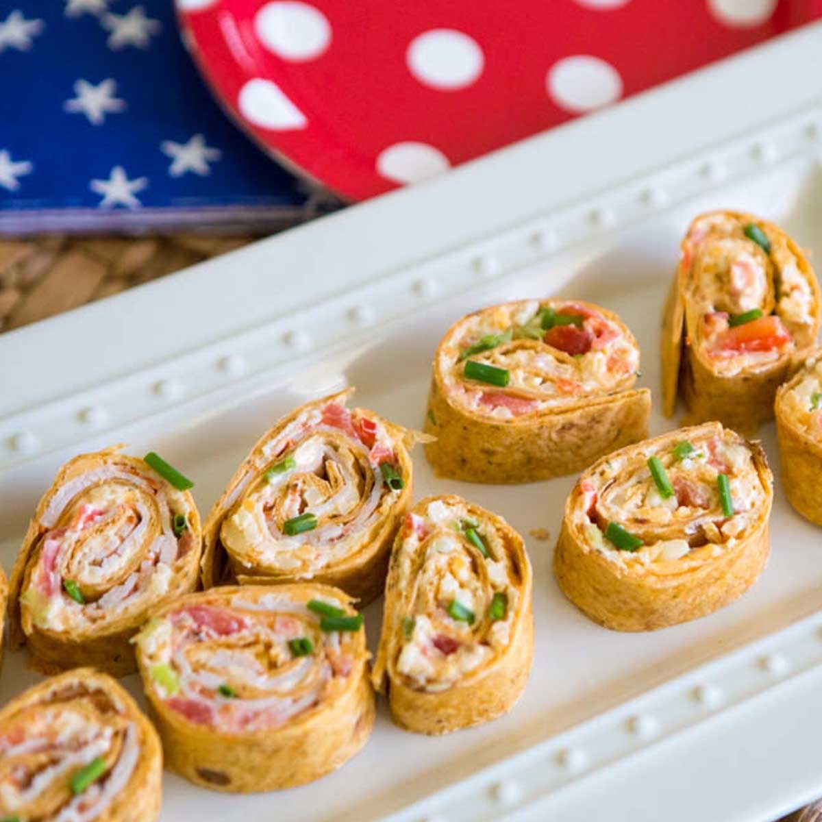 A platter of spicy firecracker pinwheels appetizers shows the meat and veggies rolled up in the tortilla.