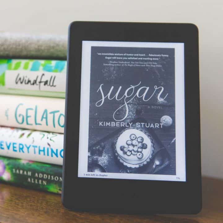 A Kindle Paperwhite is propped up against of a stack of books.