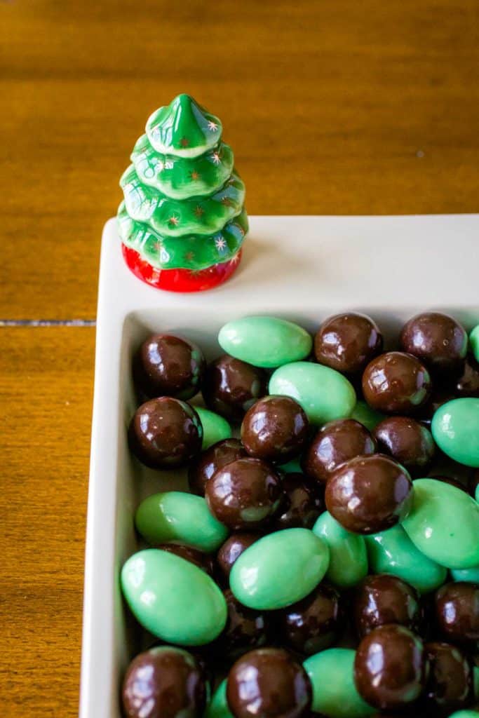 A candy dish filled with chocolates has a green ceramic Christmas tree.