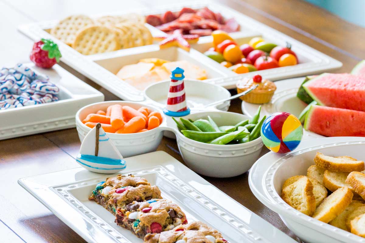 A party table is set with snacks, fruits, and cookie bars all on Nora Fleming platters.