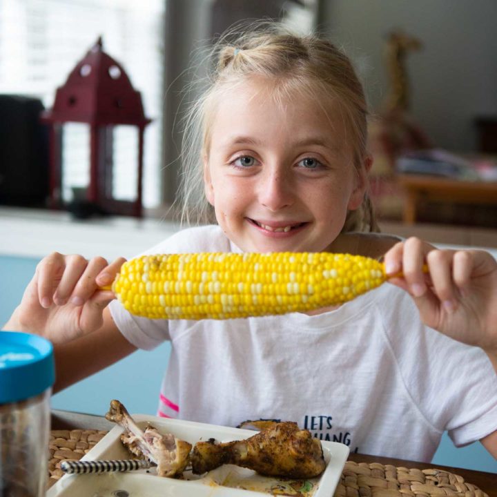 A girl holds a fresh cob of corn the night before she gets braces on.