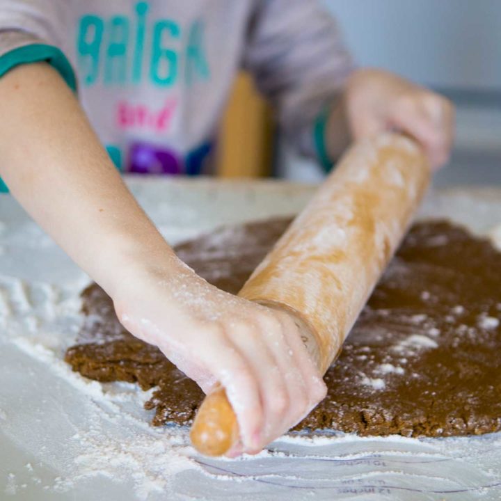 A young girl rolls out gingerbread cookie dough with a rolling pin and is covered in flour.