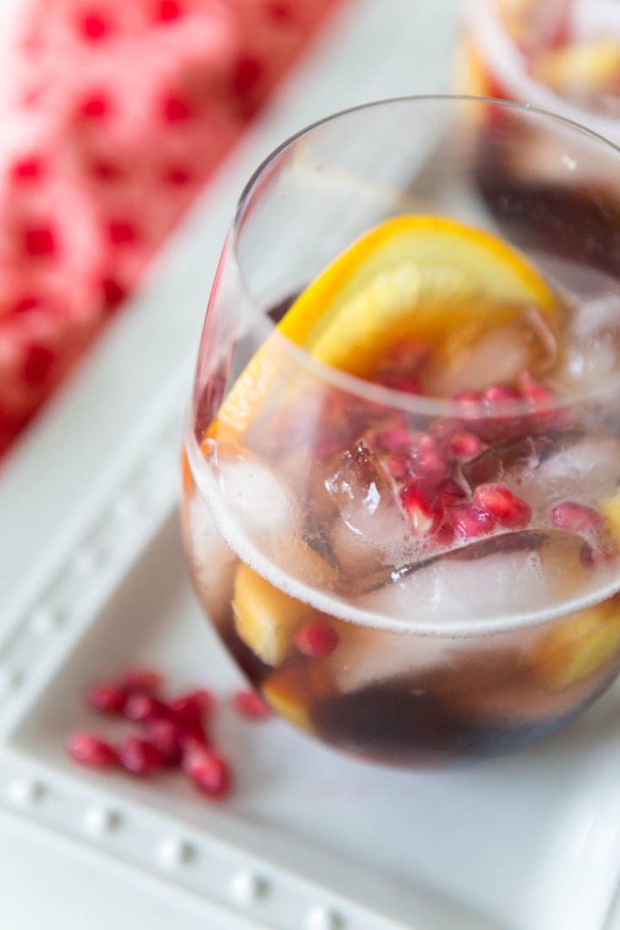 A glass of Christmas punch has slices of oranges and fresh pomegranate seeds floating in the prosecco.