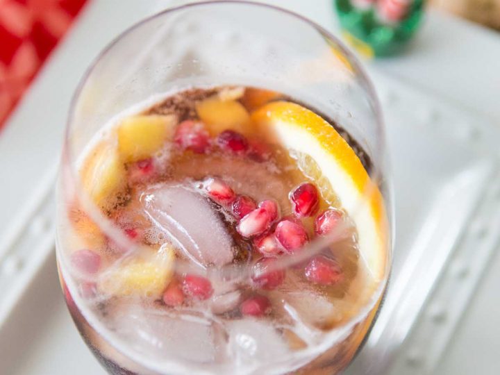 A stemless wine glass is filled with pomegranate punch, slices of fresh orange, and fresh pomegranate seeds for garnish.