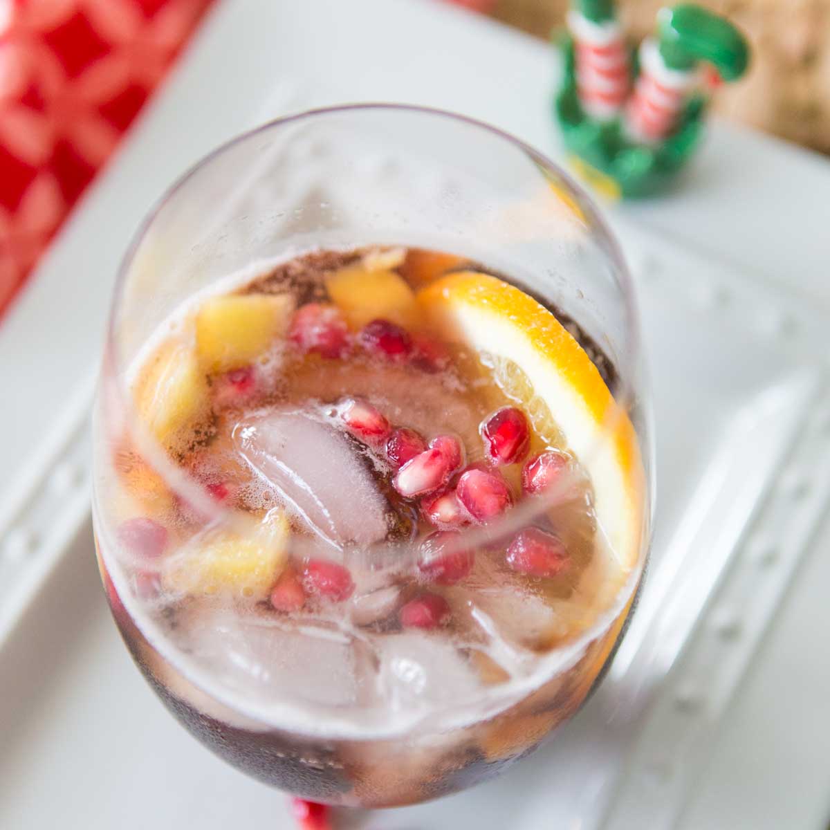 A stemless wine glass is filled with pomegranate punch, slices of fresh orange, and fresh pomegranate seeds for garnish.