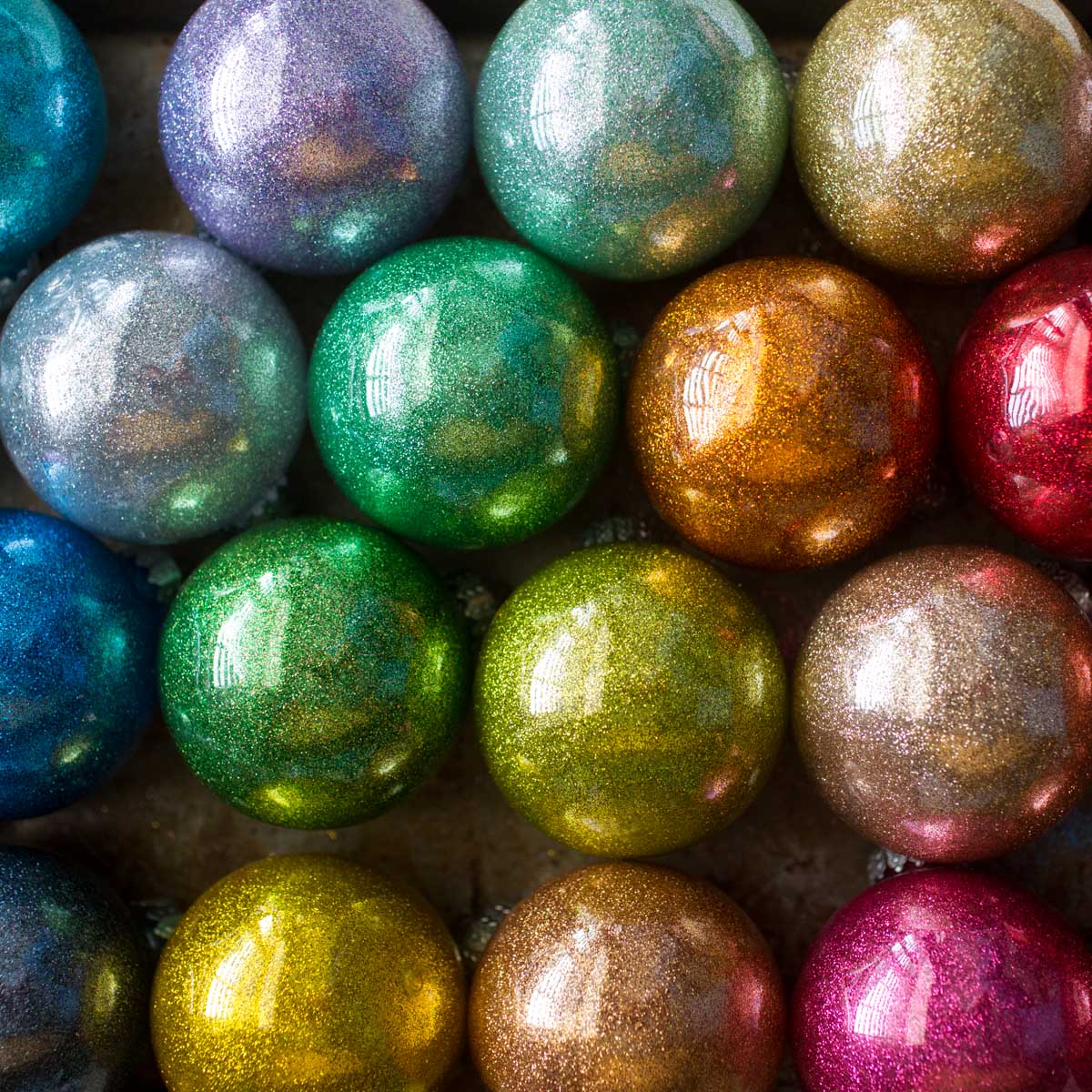 A pile of rainbow glitter ornaments are stacked on a drying tray.
