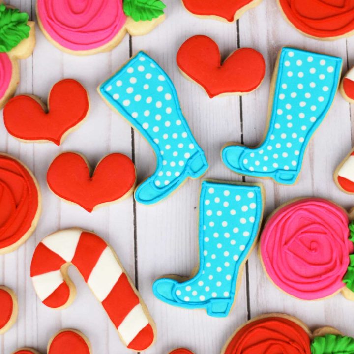 A bunch of Wellie Wishers-themed decorated sugar cookies rest on a table. Blue boots, red hearts, and striped candy cane cookies.
