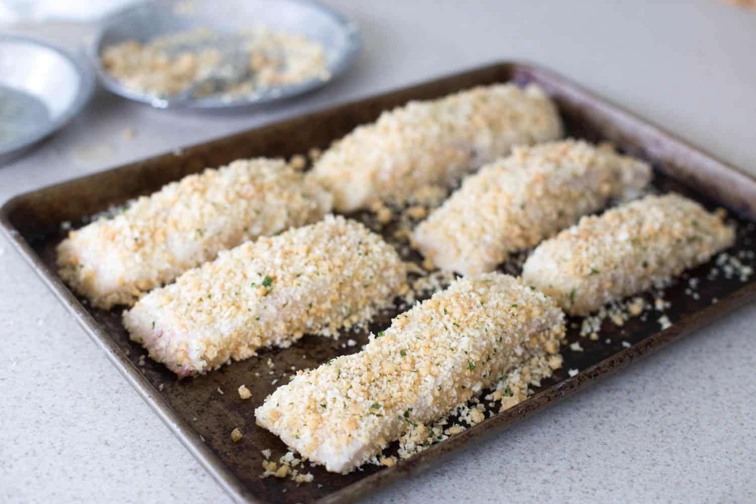 The coated fish are lined up on a baking sheet.