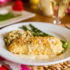 A filet of macadamia encrusted halibut is covered with a drizzle of lemon butter cream sauce. Fresh green asparagus and a serving of wild rice sit next to it on the plate.