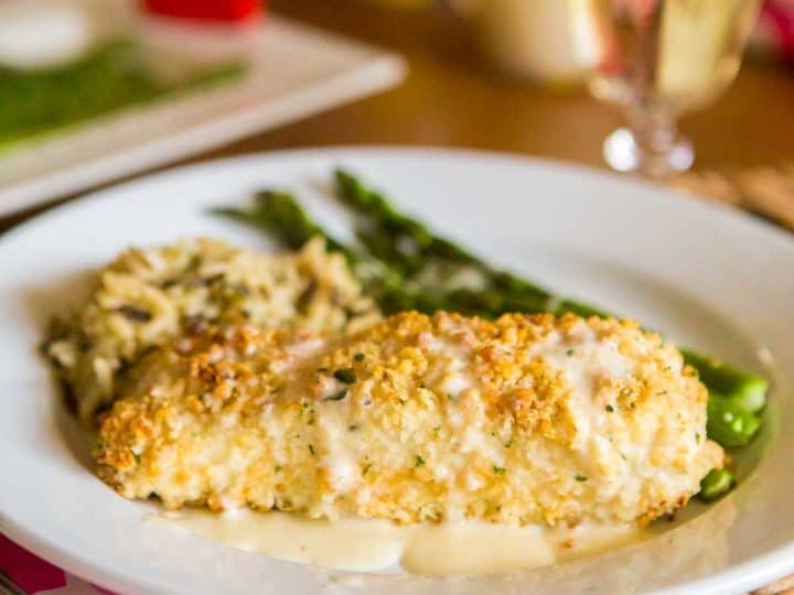 A filet of macadamia encrusted halibut is covered with a drizzle of lemon butter cream sauce. Fresh green asparagus and a serving of wild rice sit next to it on the plate.