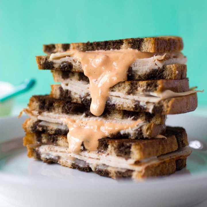 A grilled reuben sandwich is stacked in a pile and has thousand island dressing dripping down the side.
