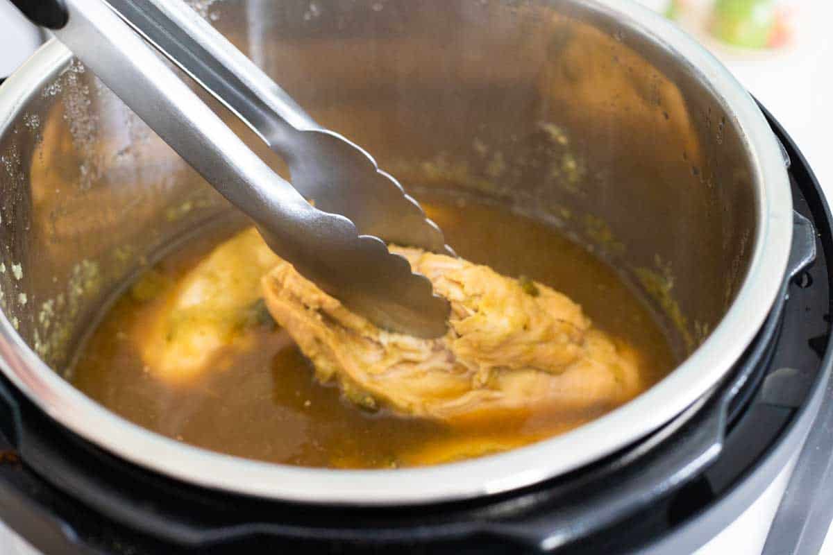 A pair of tongs is used to shred the chicken breasts right in the Instant Pot.