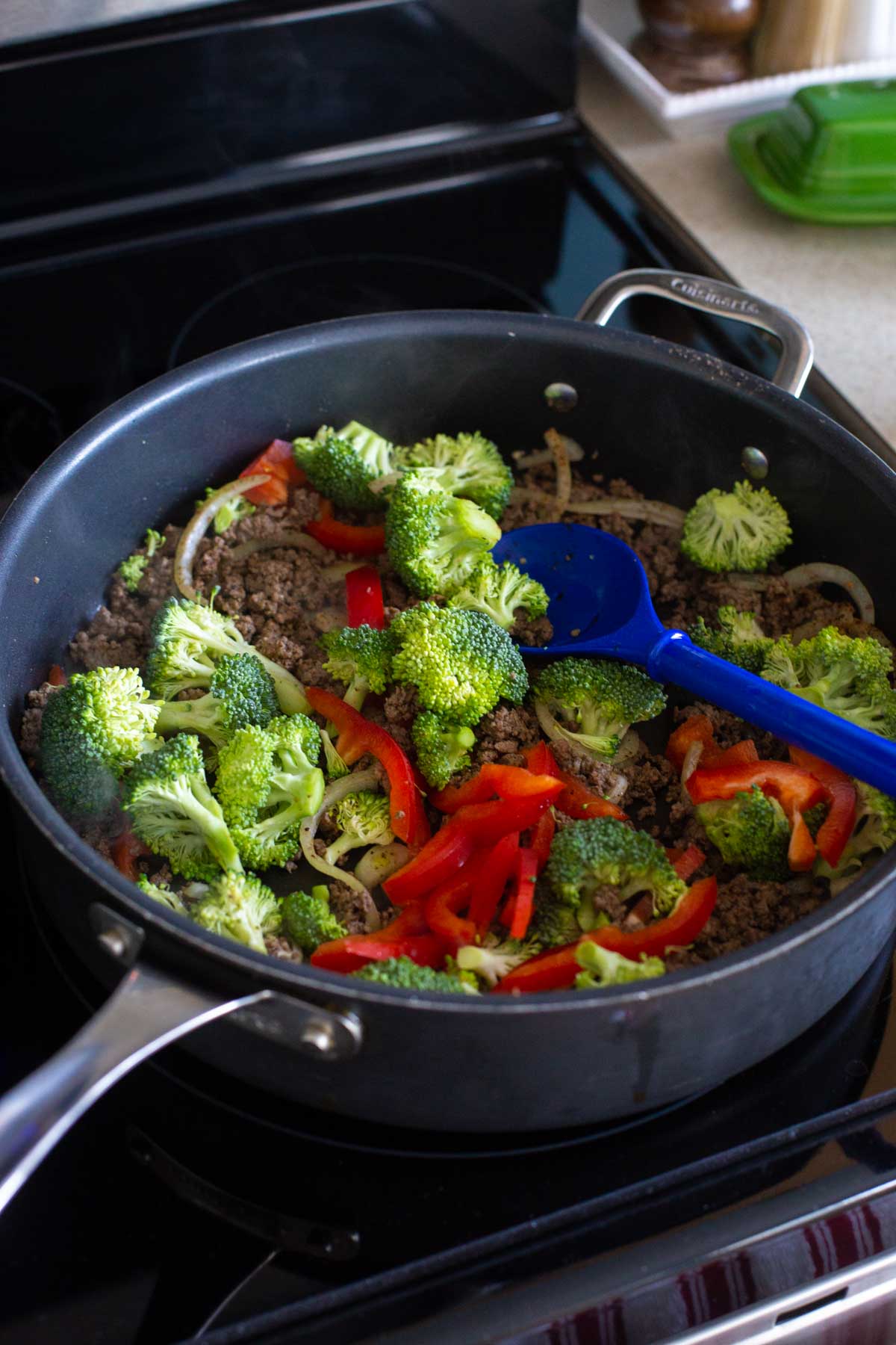 A large skillet is cooking broccoli and red peppers.