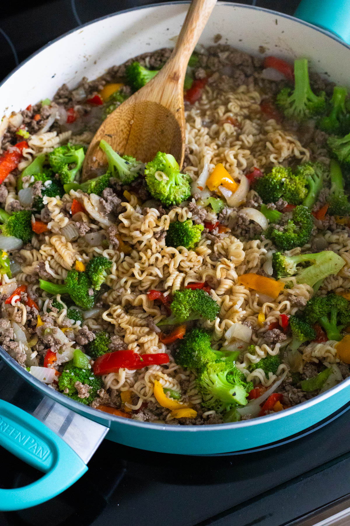 A blue skillet is filled with cooked ground beef, veggies, and ramen noodles.