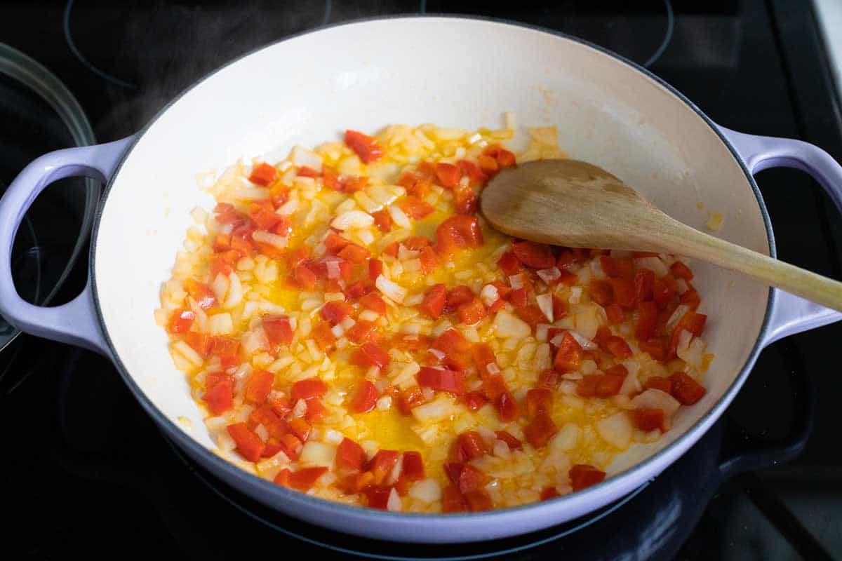 Saute pan has chopped onion and bell peppers cooking until tender.