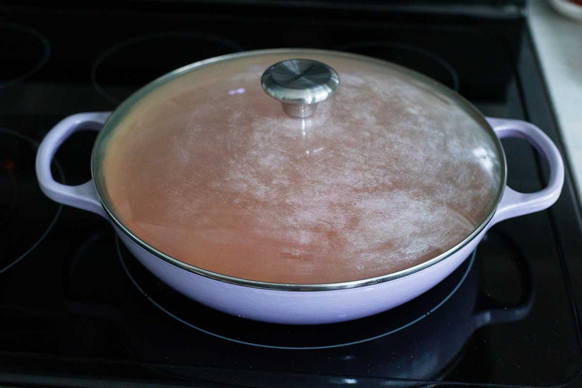 The skillet has been covered with a lid and is steaming.