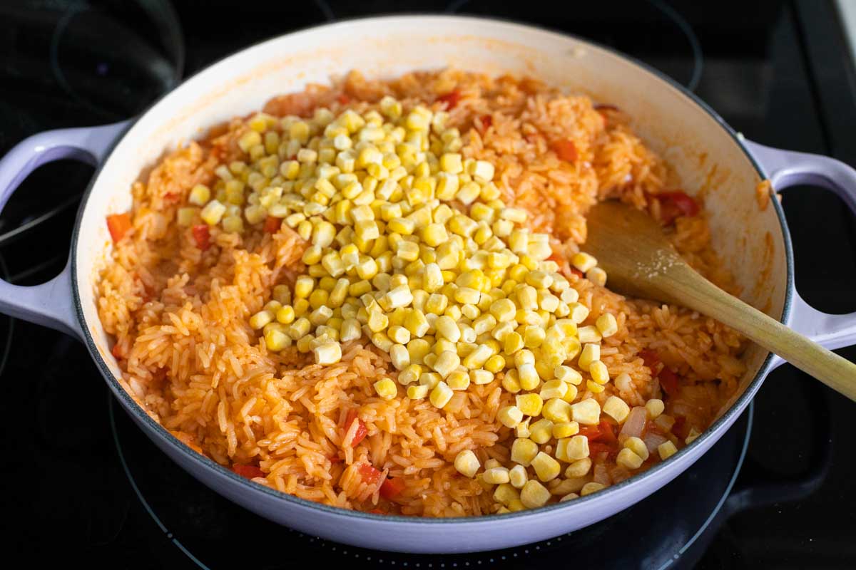 The frozen corn has been added to the cooked rice.