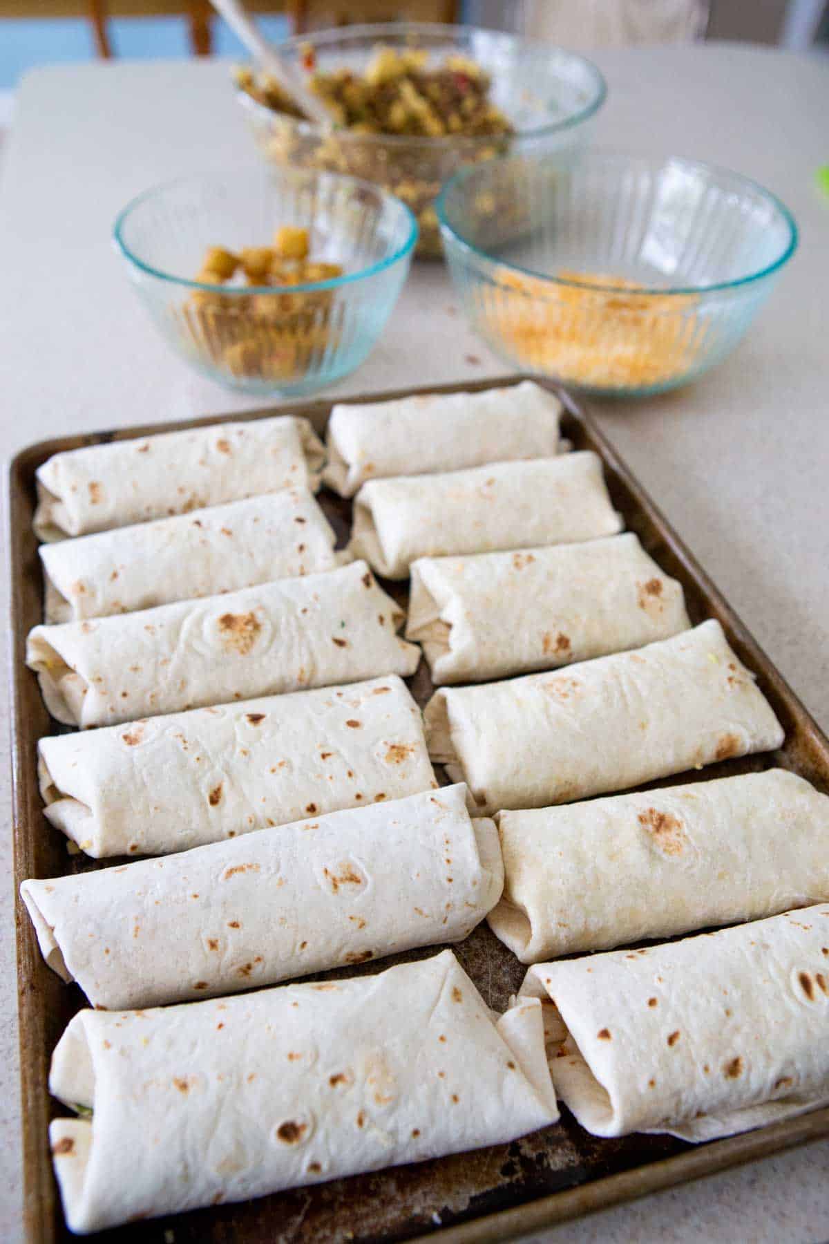 The big pan is filled with assembled burritos.