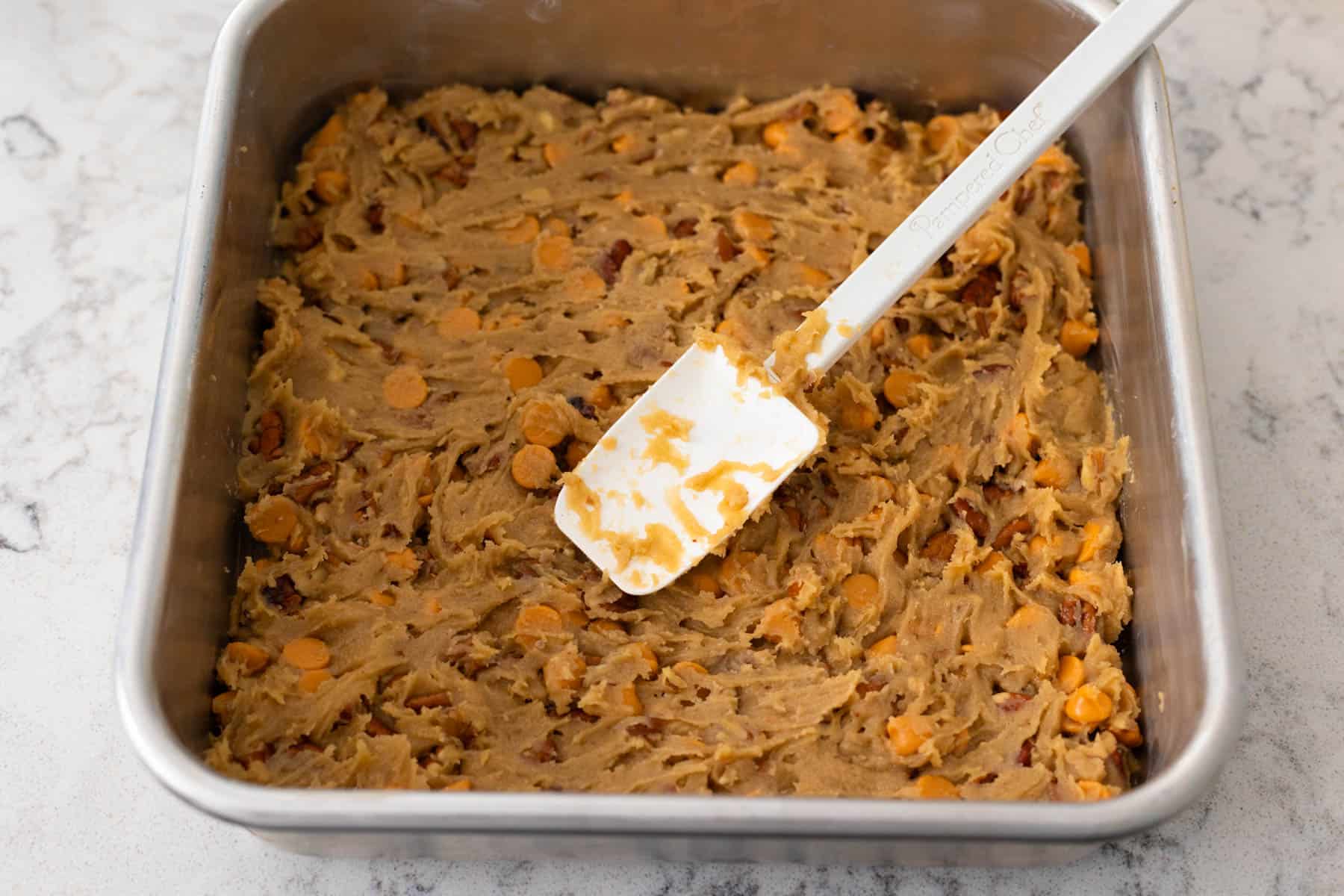 The mixed dough is being spread into a baking pan with a spatula.