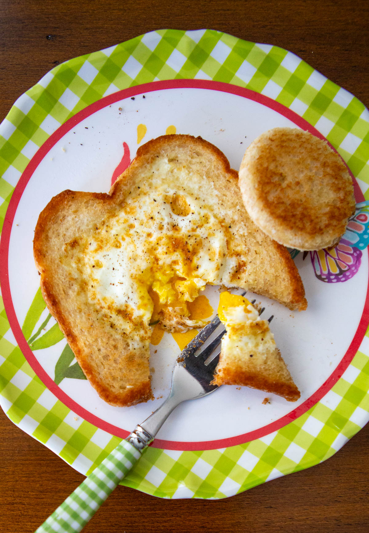 The egg in a basket toast is on a kid plate with a fork.