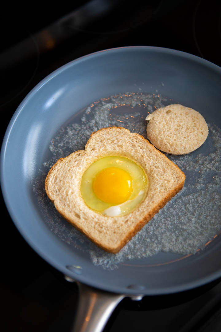 The egg has been placed inside the hole in the bread in a skillet.