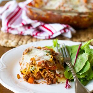 A serving of beef lasagna rollups is next to a simple green salad with a fork.