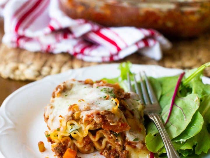 A serving of beef lasagna rollups is next to a simple green salad with a fork.