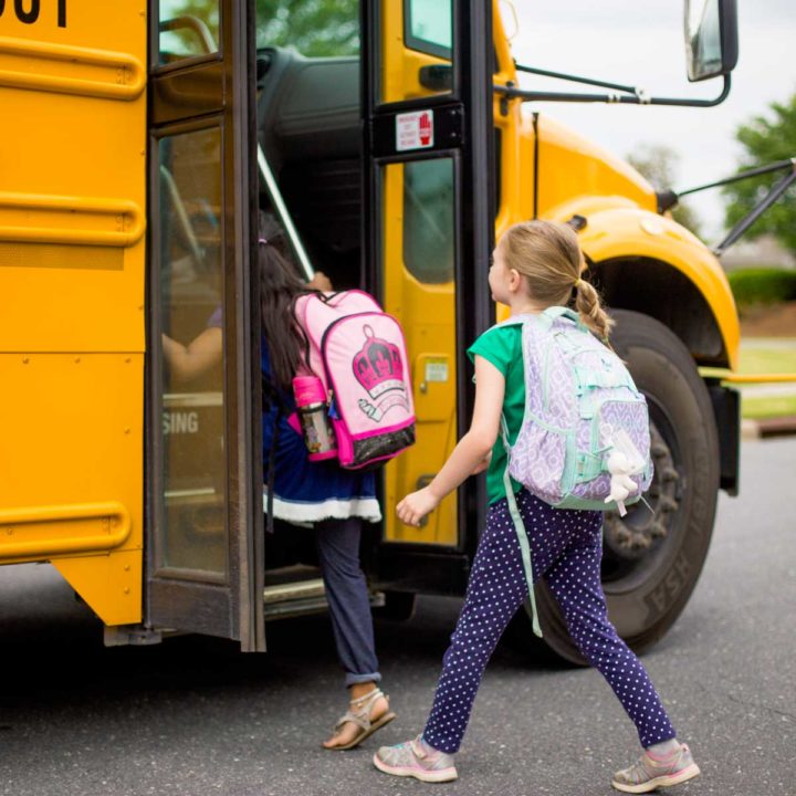 A young girl gets on a yellow school bus on the first day of school.