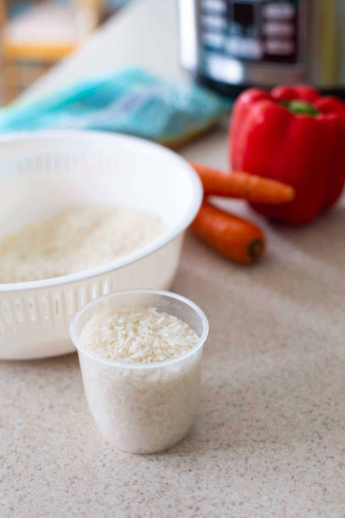 A measuring cup filled with white rice is by the Instant Pot.