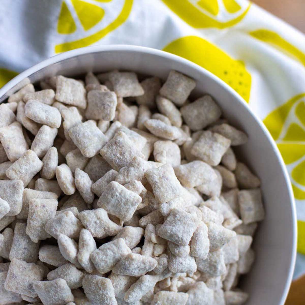 A bowl of powdered sugar coated Chex cereal next to a napkin with lemons on it.