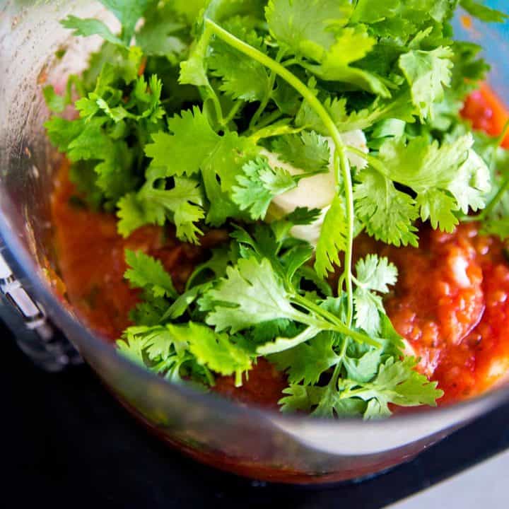 Fresh cilantro is about to be mixed into a homemade salsa recipe inside a food processor.