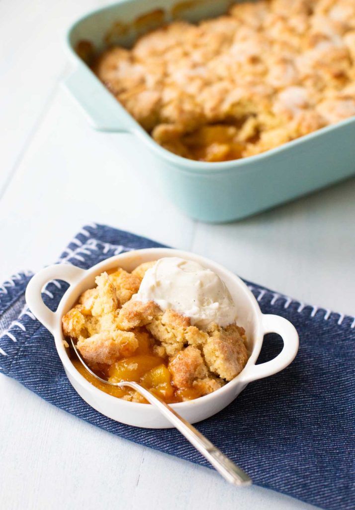 Finished peach cobbler with a serving topped with ice cream.